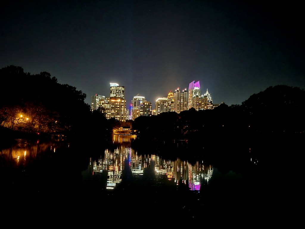 Night view of the Houston city skyline reflecting on a calm body of water, with illuminated buildings showcasing various colors.